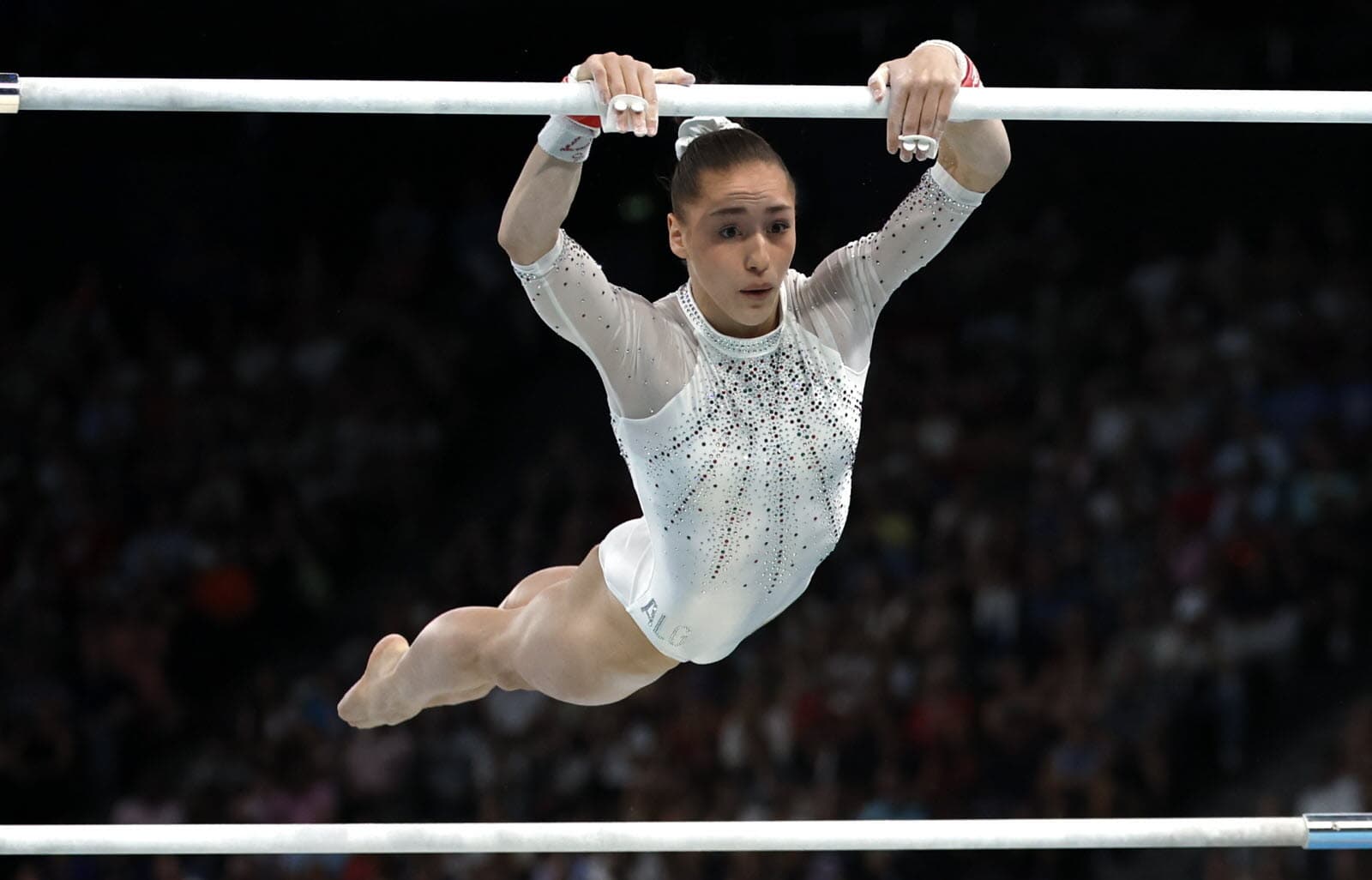 Gymnaste féminine effectuant une figure sur la barre asymétrique.