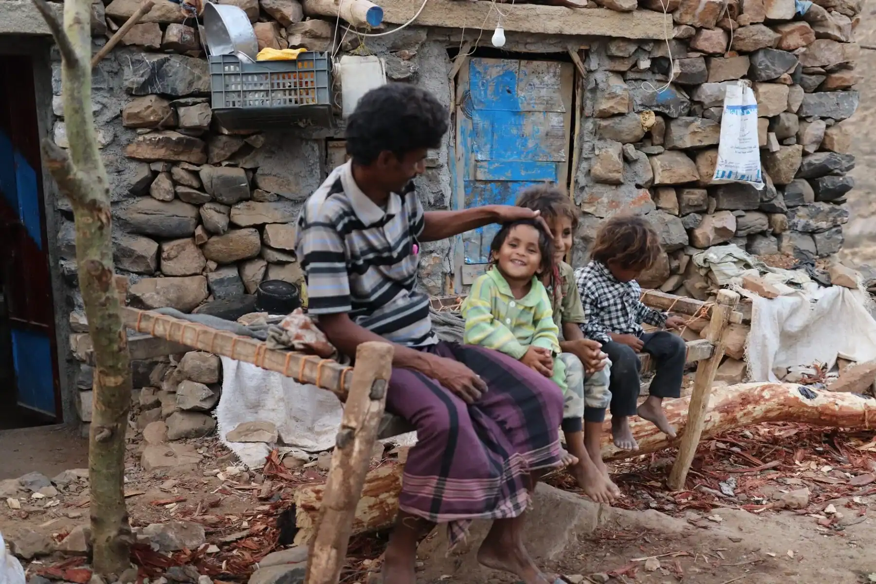 Famille dans un environnement pauvre au Maroc, enfants assis sur un banc en bois.