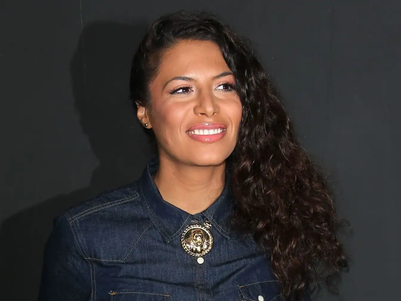 Zaho souriante avec cheveux bouclés, vêtue d'une veste en denim.