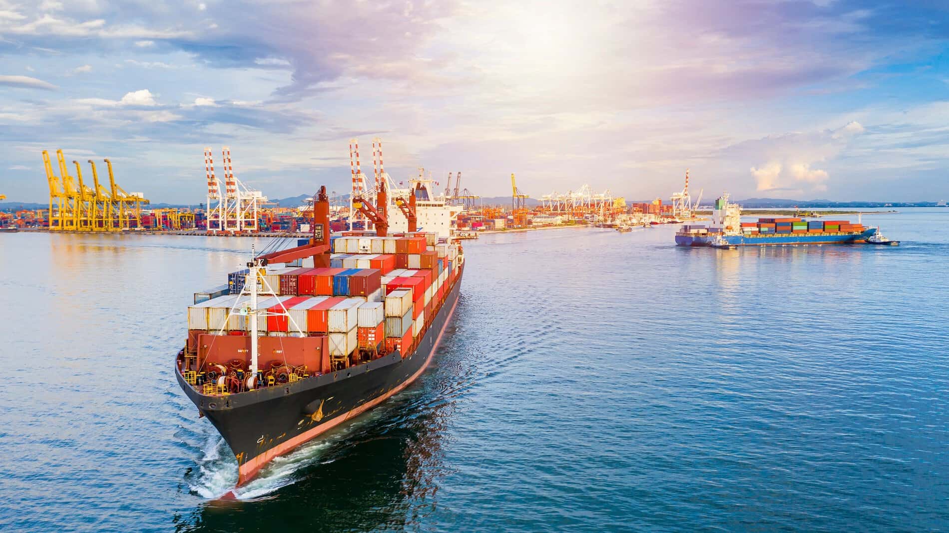 Navire de conteneurs en mer avec port industriel en arrière-plan.
