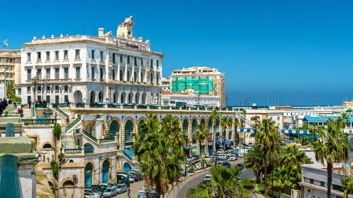 Découvrez le guide ultime pour un weekend inoubliable à Alger ! Vue d'Alger avec bâtiments historiques et palmiers sous ciel bleu clair.