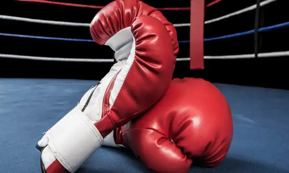 Découvrez comment Besma Bahri a brillé aux JO de la jeunesse ! Équipement de boxe avec gants et casque dans un ring.