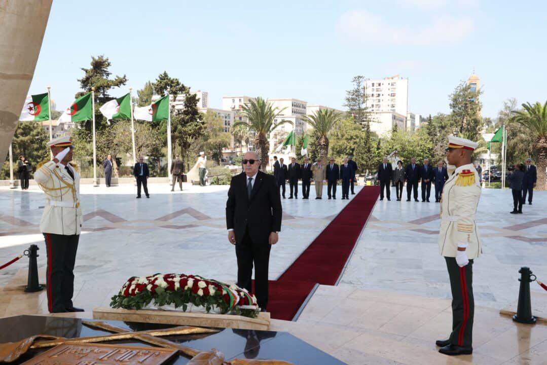Cérémonie officielle en Algérie avec drapeaux et soldats en uniforme.