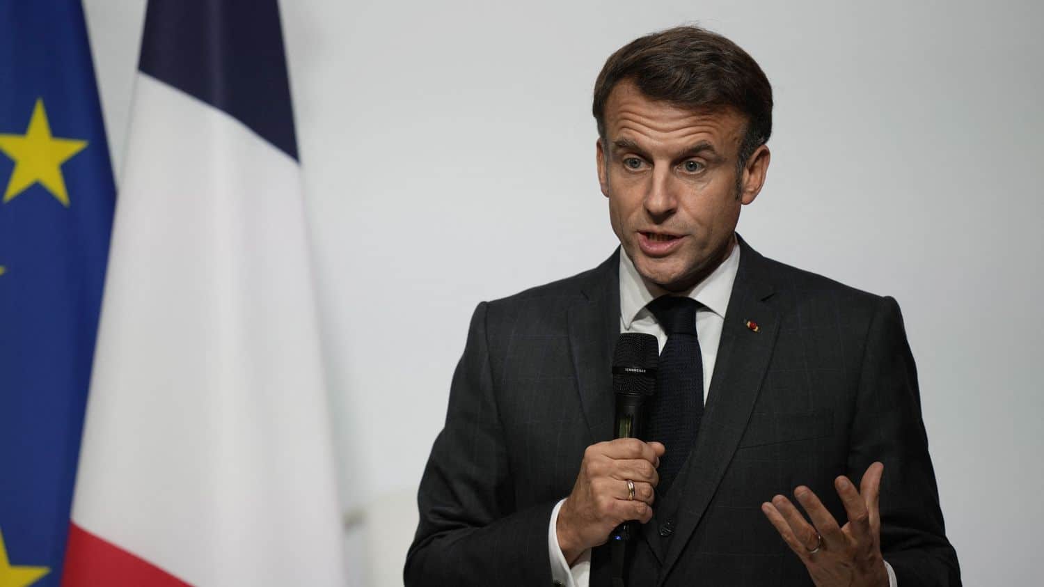 Macron lors d'une déclaration officielle Emmanuel Macron parlant lors d'une conférence, drapeau français en arrière-plan.
