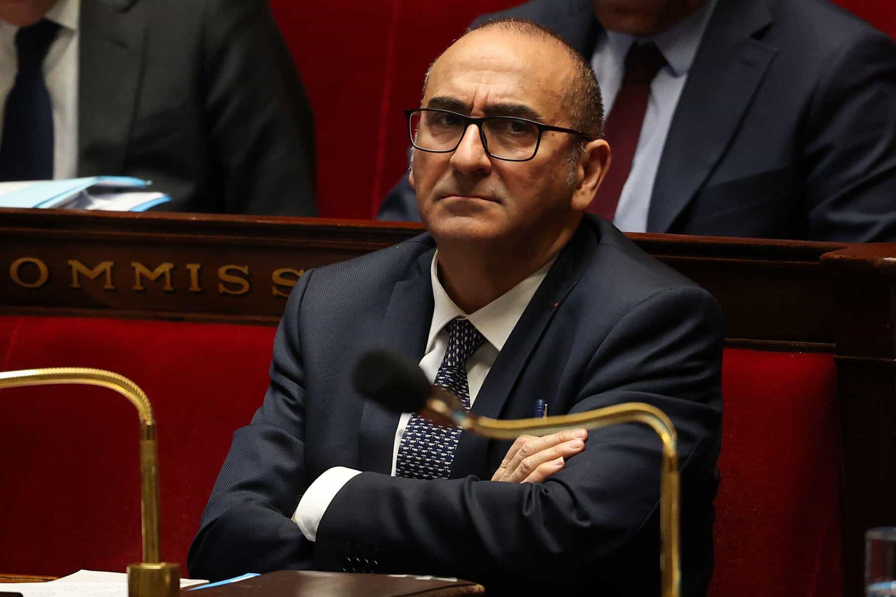 Député lors d'une session parlementaire Homme politique en séance parlementaire, portant costume et lunettes.