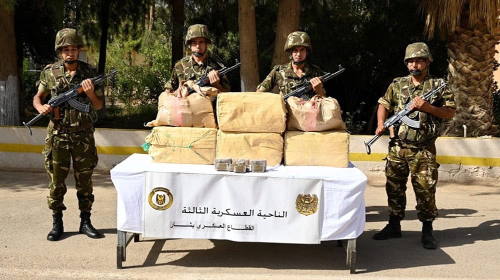Découverte choc : L’armée algérienne saisit une tonne de drogue Soldats armés algériens devant des sacs de drogue saisie.