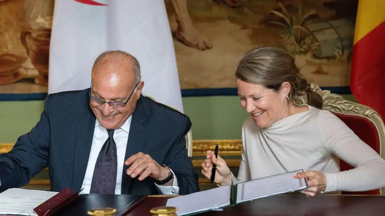 Belgique–Algérie : un pacte migratoire pour débloquer les expulsions Deux personnes signent un accord migratoire dans une salle officielle.