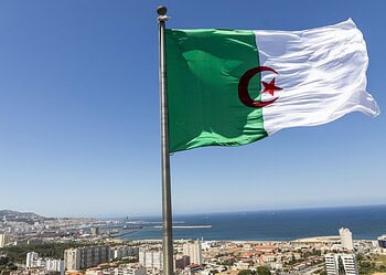 Drapeau algérien flottant dans le ciel avec vue sur la ville et la mer.