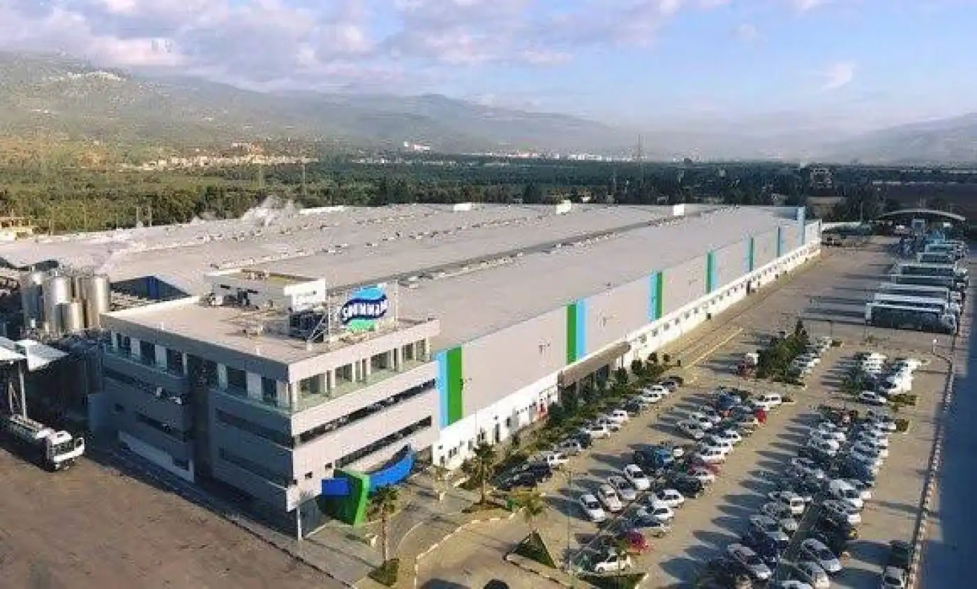 Soummam : un investissement de 4 milliards DA qui change tout Grande usine industrielle avec parking spacieux et paysage montagneux en arrière-plan.