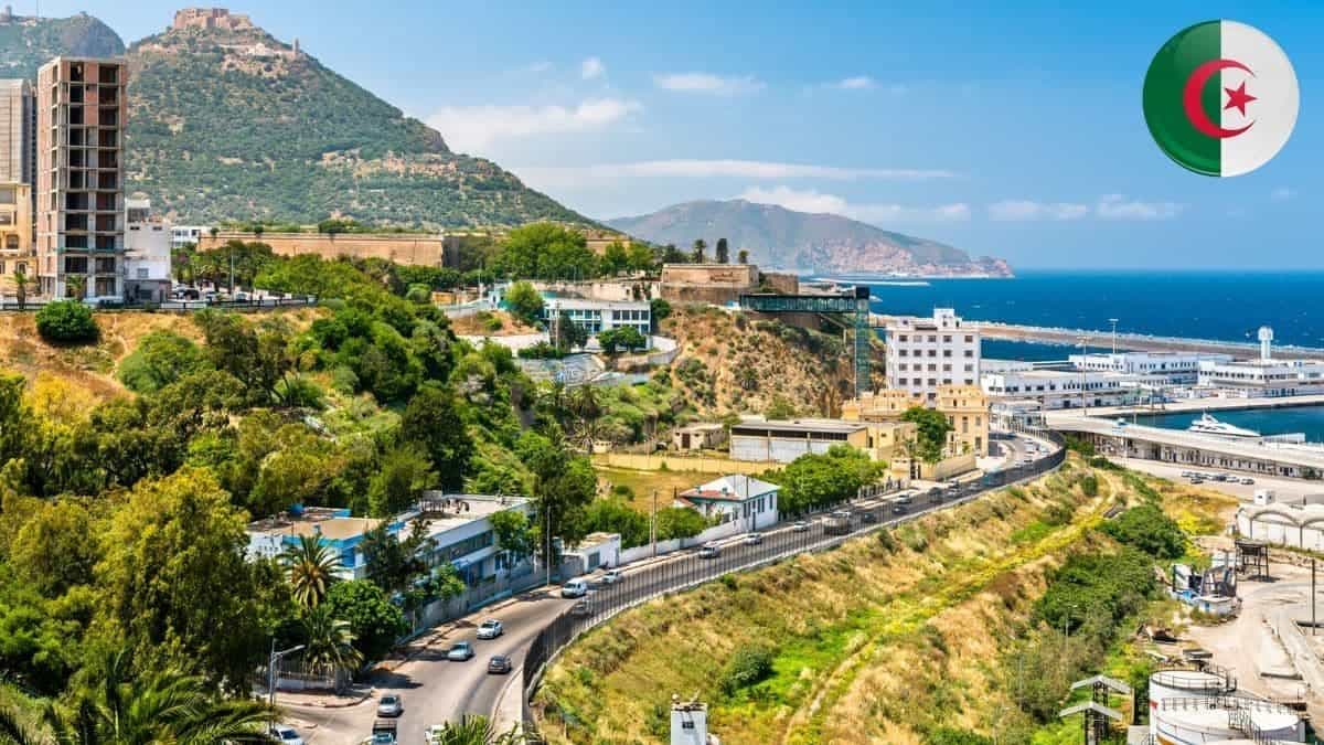 Inscrivez votre enfant pour des vacances gratuites en Algérie en 2026 ! Paysage urbain d'Alger avec mer, montagnes et drapeau algérien.