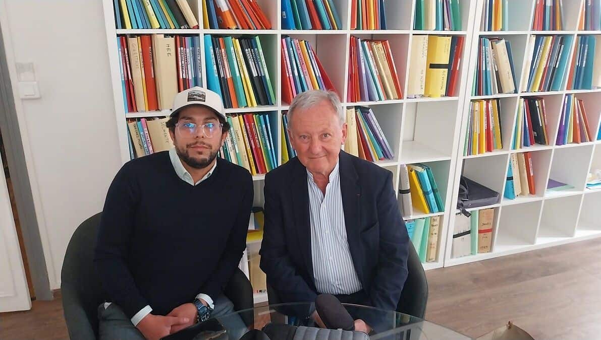 Expulsion controversée : un Algérien malade face à l’OQTF Deux hommes assis à une table en bibliothèque, livres en arrière-plan.