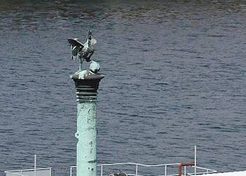 Statue de pélican en métal sur un poteau au bord de l'eau.