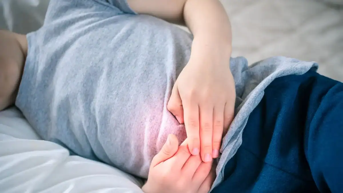 Enfant allongé sur le lit avec douleur abdominale visible.