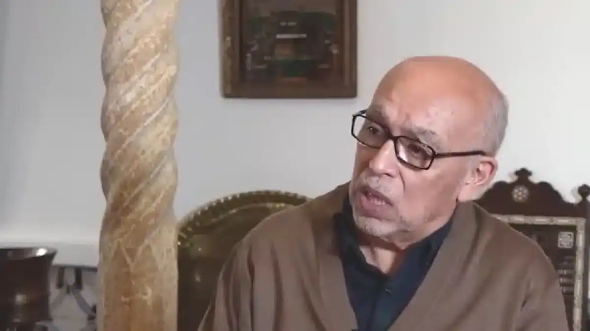 Pourquoi la France a-t-elle perdu son expertise en Algérie ? Homme âgé parlant, lunettes, intérieur classique, contexte historique.