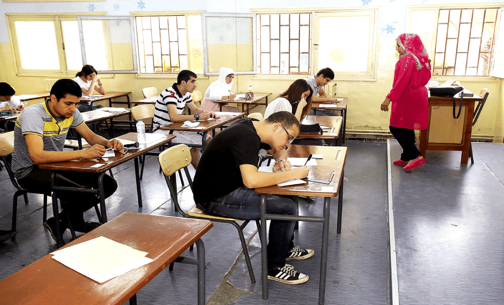 Étudiants en examen dans une salle de classe avec une enseignante.