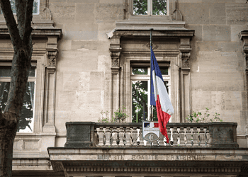 Drapeau français devant un bâtiment officiel historique.
