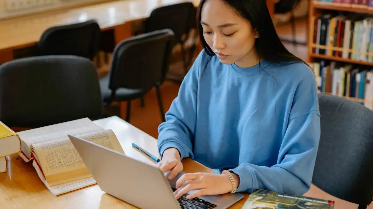 Frais étudiants étrangers en France : hausse choc dès 2026 Jeune femme étudiant à la bibliothèque avec ordinateur et livres.