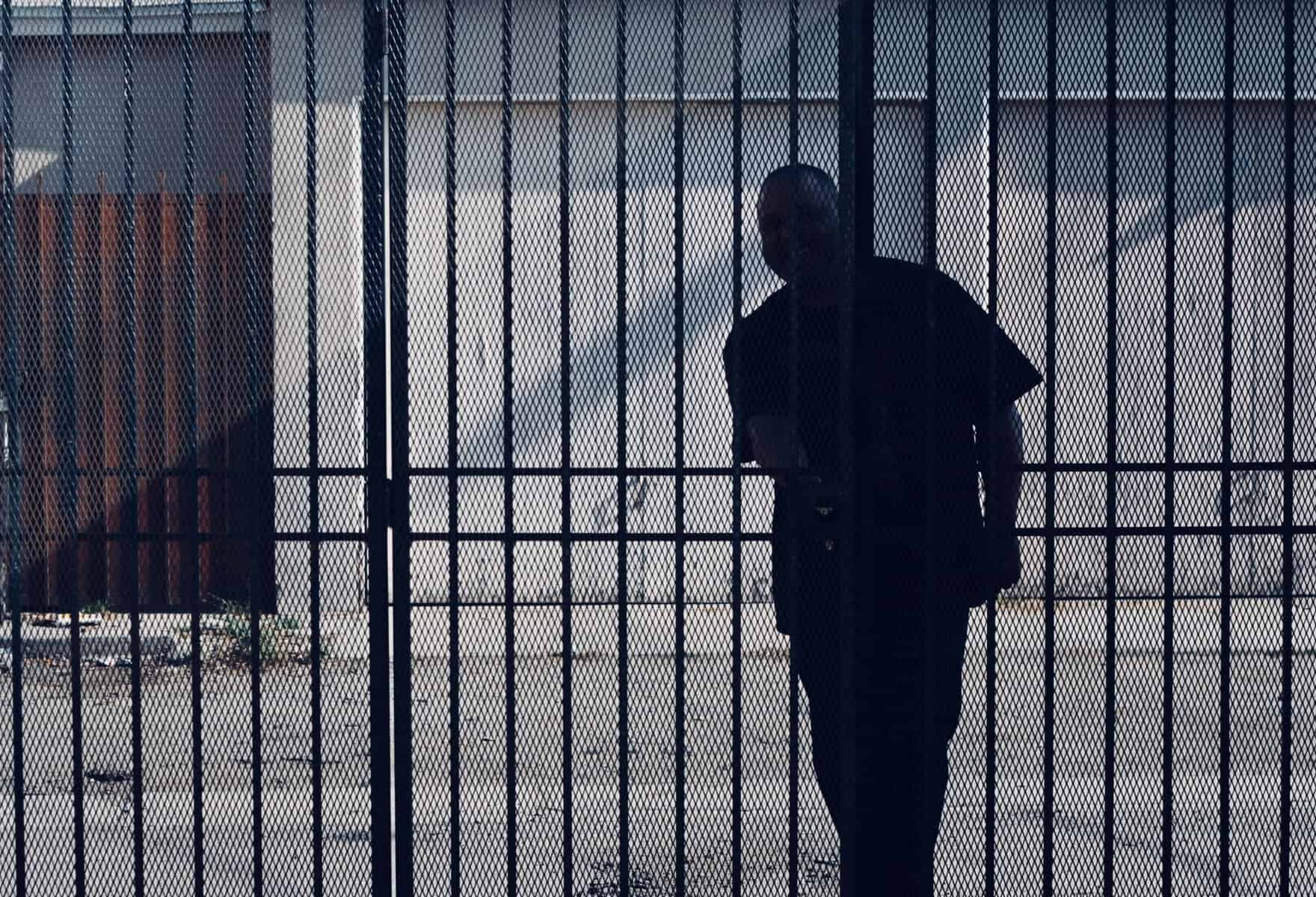 Homme en silhouette derrière une grille de prison ou de centre de rétention.